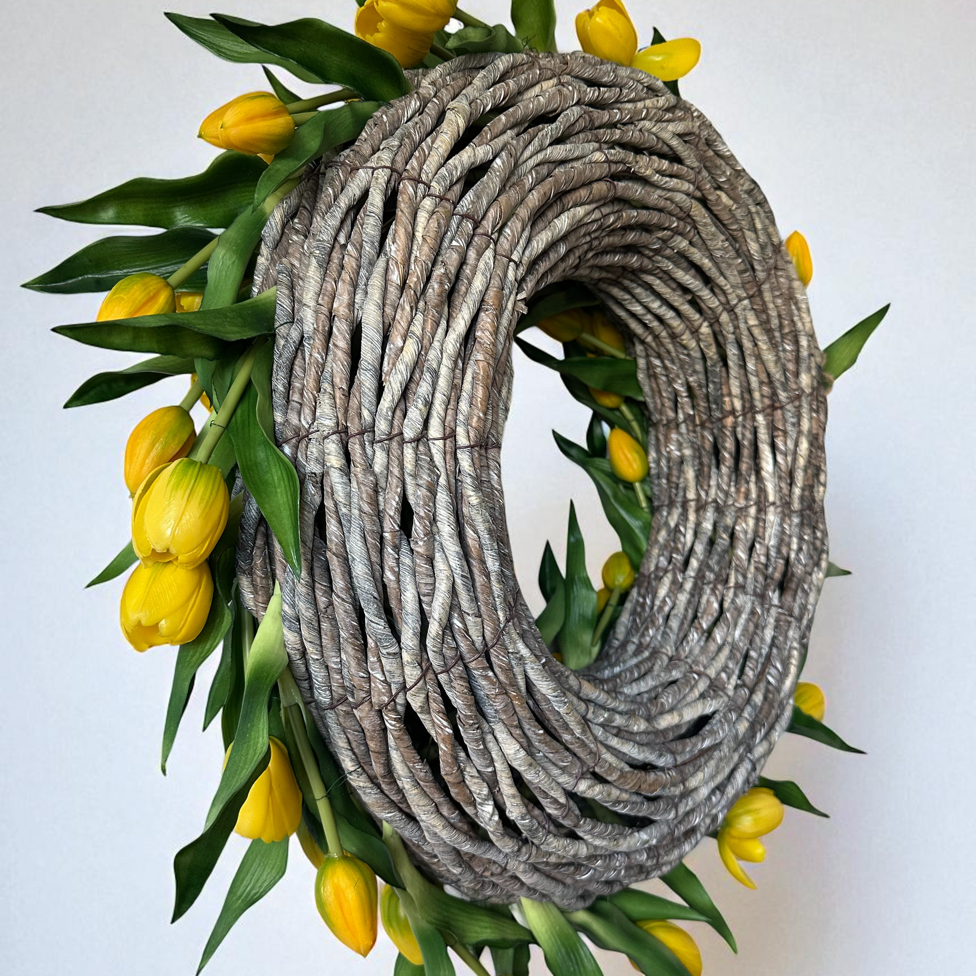 Handgemaakte luxe deurkrans met heldere gele kunsttulpen, kunstig gerangschikt op een natuurlijke, gevlochten takkenbasis. Deze opvallende tulpenkrans van Jardin Enchanté brengt direct zonneschijn en een warme, vrolijke uitstraling naar uw voordeur of interieur. Perfect als seizoensdecoratie voor de lente en zomer, en ideaal voor wie op zoek is naar een unieke luxe kunstbloemenkrans of stijlvolle deurdecoratie. Deze exclusieve krans combineert elegantie en levendige kleuren om een uitnodigende en verfijnde