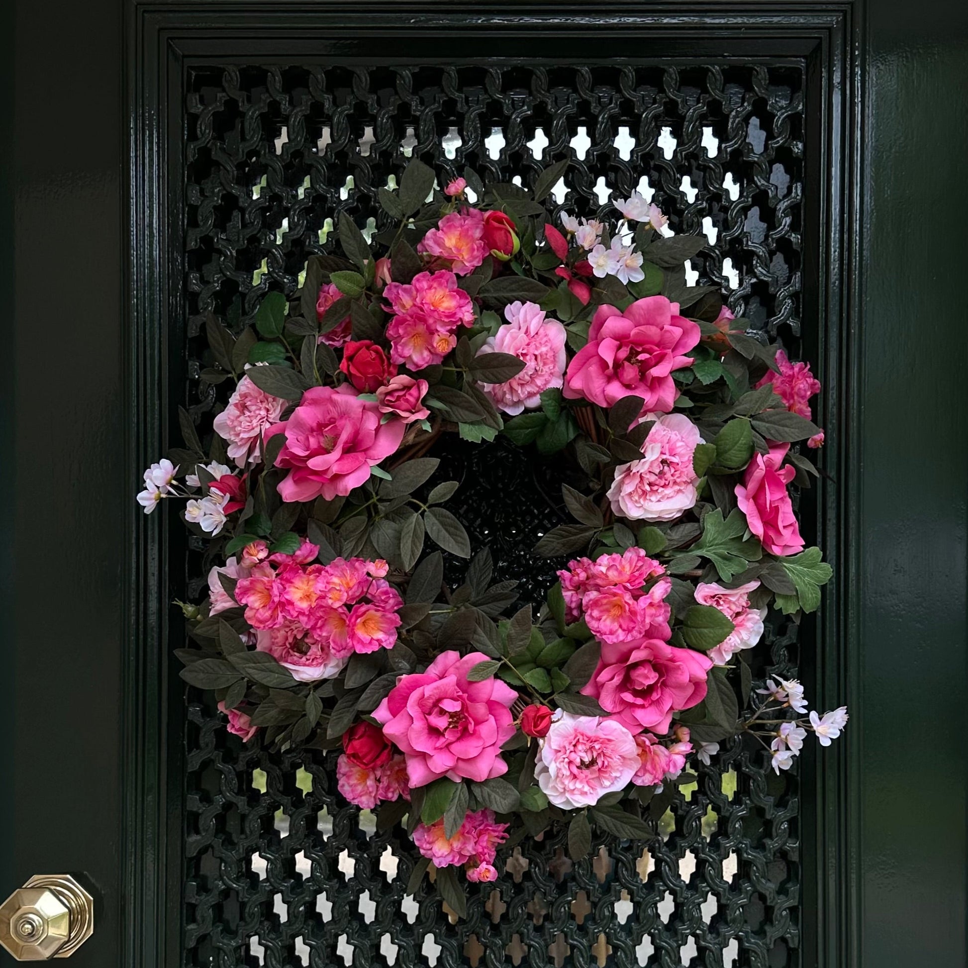 Handgemaakte luxe deurkrans met roze en fuchsia kunstrozen, pioenrozen en ranonkels op een groene, natuurlijke ondergrond — Jardin Enchanté.
