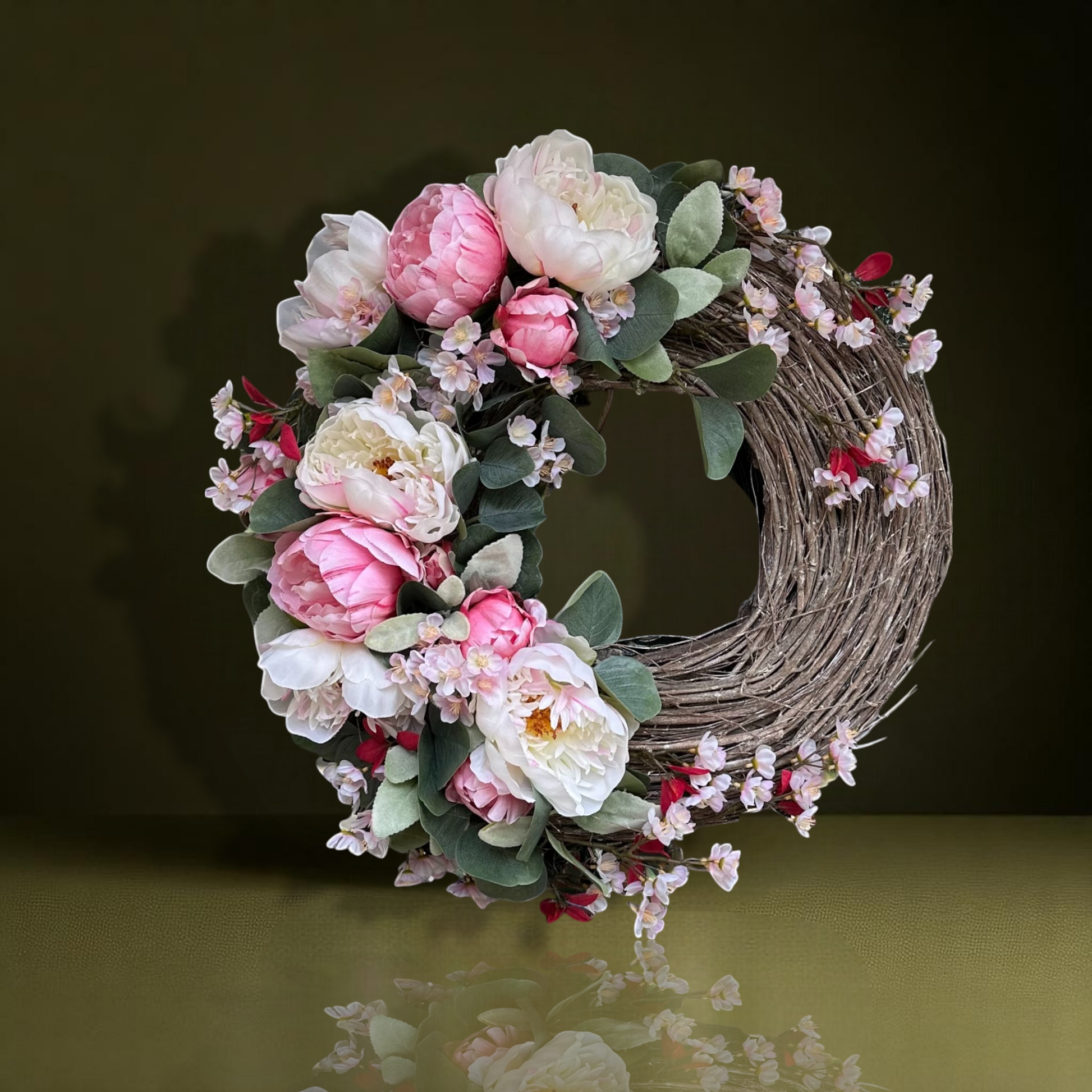 Handgemaakte luxe deurkrans met zijden pioenrozen in zachte blushroze en crèmekleurige tinten, gecombineerd met kunst kersenbloesems en fluweelachtig groen blad, zorgvuldig gerangschikt op een natuurlijke takkenbasis. Deze romantische, asymmetrische bloemenkrans van Jardin Enchanté straalt Franse elegantie en verfijnde charme uit. Perfect als luxe kunstbloemenkrans voor de voordeur, muurdecoratie of feestelijke gelegenheid, en ideaal voor liefhebbers van romantische, exclusieve seizoensdecoratie.