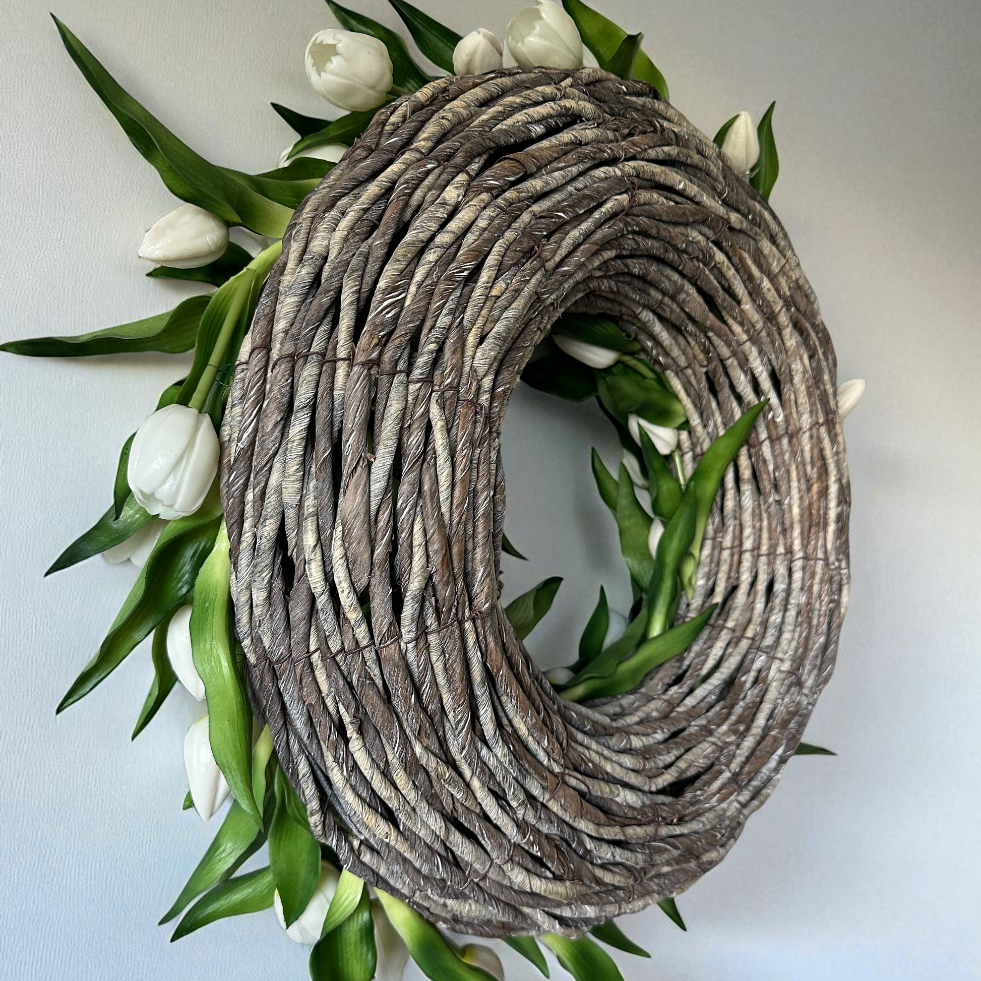 Handgemaakte luxe deurkrans met elegante witte kunsttulpen, zorgvuldig gerangschikt op een natuurlijke gevlochten basis van takken, perfect voor een stijlvolle voordeurdecoratie of als muurdecoratie binnenshuis. Deze exclusieve tulpenkrans van Jardin Enchanté straalt tijdloze verfijning en een romantische, frisse uitstraling uit. Ideaal voor wie op zoek is naar een bijzondere seizoensdecoratie, lente- of zomerkrans, of luxe kunstbloemen krans voor een warm en uitnodigend huis.