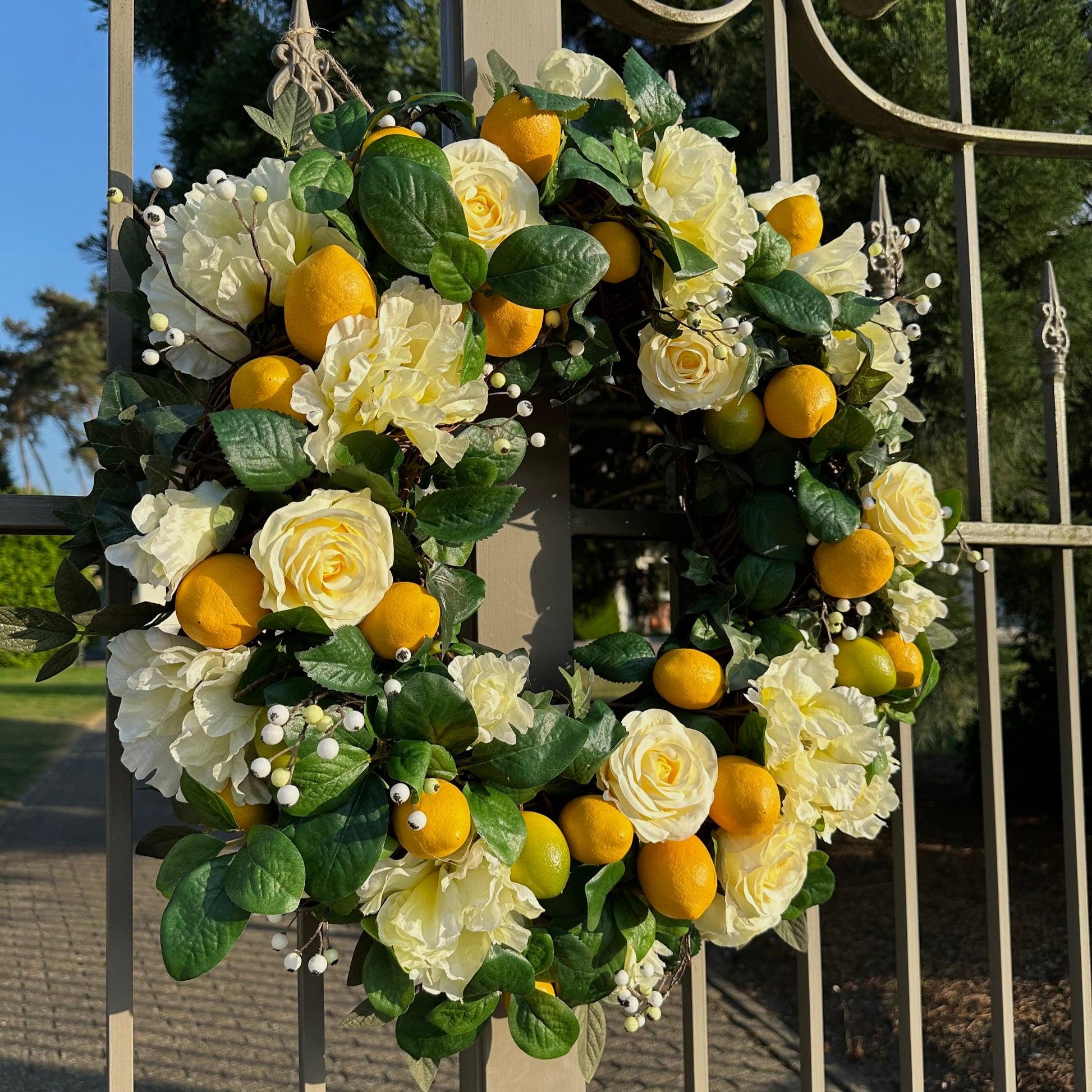 Handgemaakte luxe deurkrans van Jardin Enchanté met elegante zachtgele kunstrozen, speelse citroenen, delicate witte bessen en weelderig groene bladeren op een natuurlijke basis. Deze stijlvolle krans brengt een frisse mediterrane uitstraling en zonnige charme naar elke deur of muur en is perfect als zomerse decoratie voor een warm en uitnodigend huis.