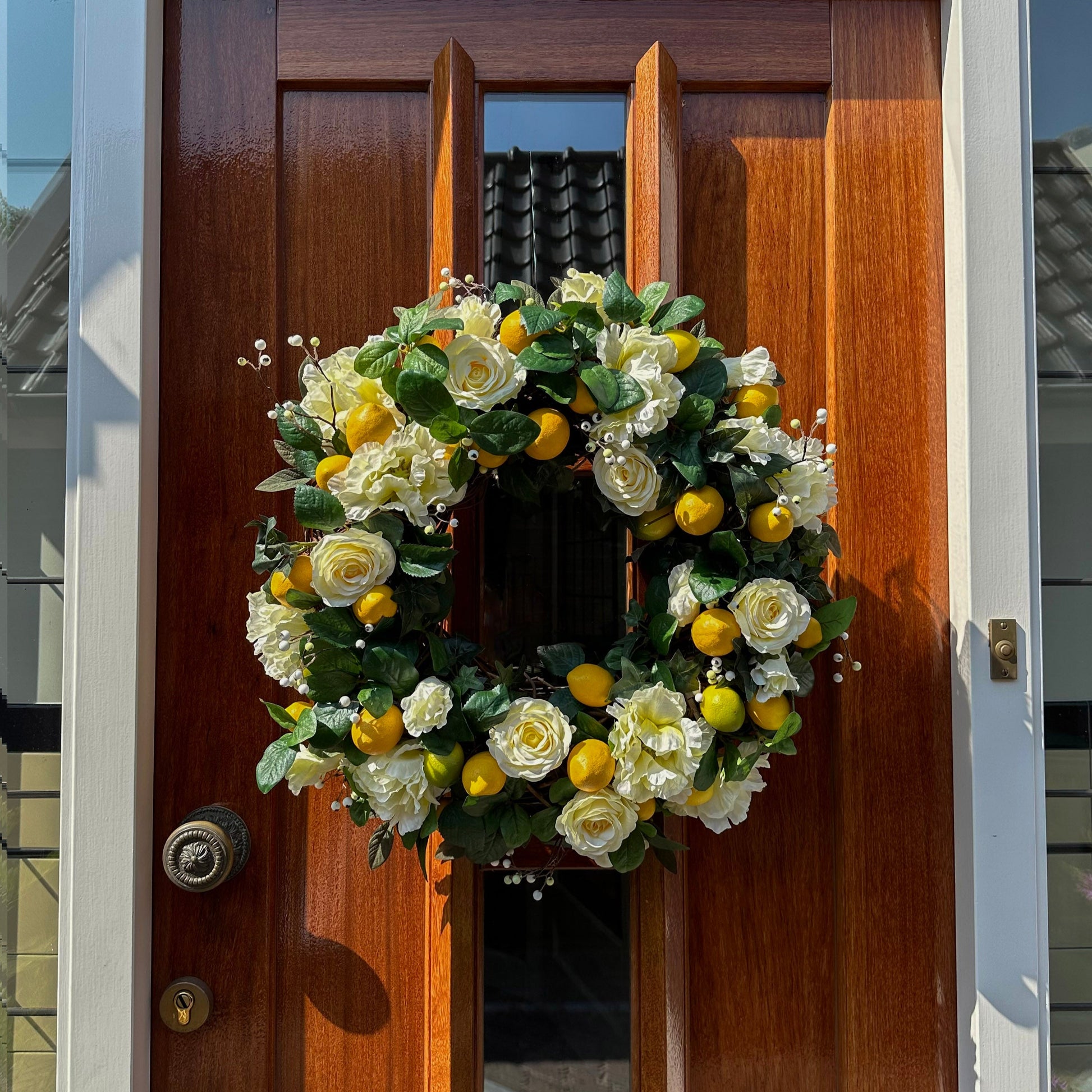 Handgemaakte luxe deurkrans van Jardin Enchanté met elegante zachtgele kunstrozen, speelse citroenen, delicate witte bessen en weelderig groene bladeren op een natuurlijke basis. Deze stijlvolle krans brengt een frisse mediterrane uitstraling en zonnige charme naar elke deur of muur en is perfect als zomerse decoratie voor een warm en uitnodigend huis.