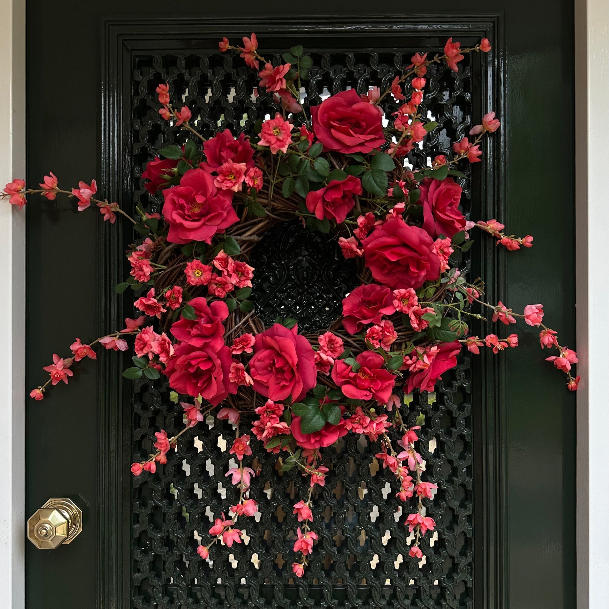 Handgemaakte luxe deurkrans met felle rode en fuchsia kunstrozen, delicate kersenbloesems en levendig groen blad, speels en asymmetrisch gerangschikt op een natuurlijke basis van takken. Deze expressieve bloemenkrans van Jardin Enchanté straalt passie, romantiek en mediterrane flair uit. Perfect als opvallende kunstbloemenkrans voor de voordeur, muurdecoratie of feestelijke gelegenheden. Ideaal voor wie een elegante, luxe seizoensdecoratie zoekt die direct een statement maakt.