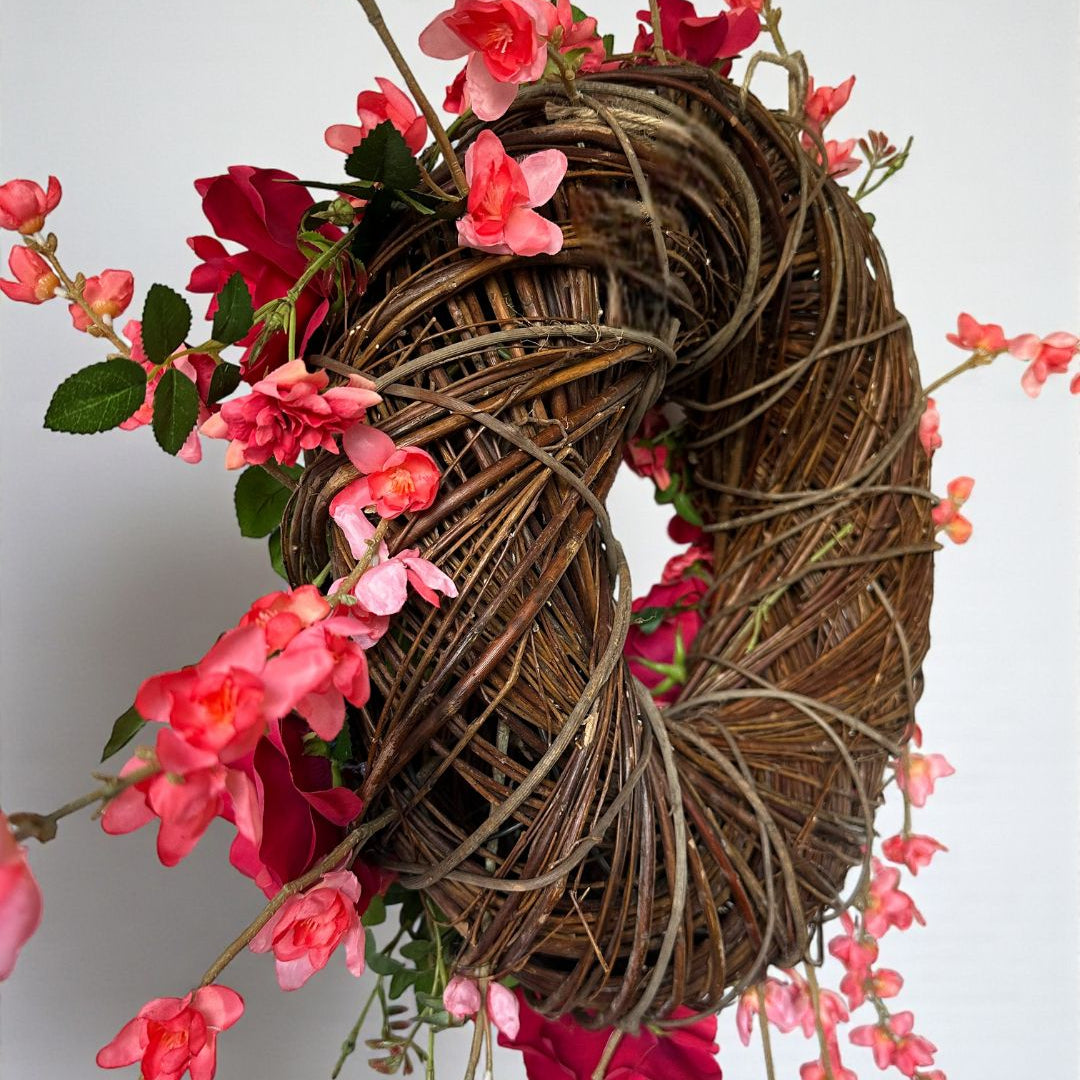 Handgemaakte luxe deurkrans met felle rode en fuchsia kunstrozen, delicate kersenbloesems en levendig groen blad, speels en asymmetrisch gerangschikt op een natuurlijke basis van takken. Deze expressieve bloemenkrans van Jardin Enchanté straalt passie, romantiek en mediterrane flair uit. Perfect als opvallende kunstbloemenkrans voor de voordeur, muurdecoratie of feestelijke gelegenheden. Ideaal voor wie een elegante, luxe seizoensdecoratie zoekt die direct een statement maakt.