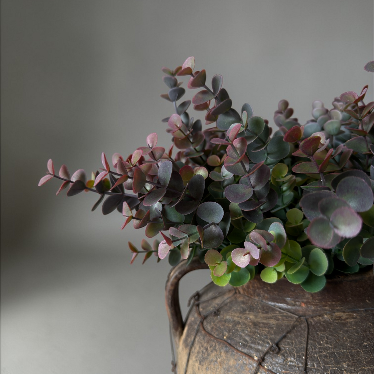 Dusky Eucalyptus Boeket, een luxe zijden eucalyptus boeket met gedempte groene en zachte bordeaux tinten in een rustieke aardewerken vaas