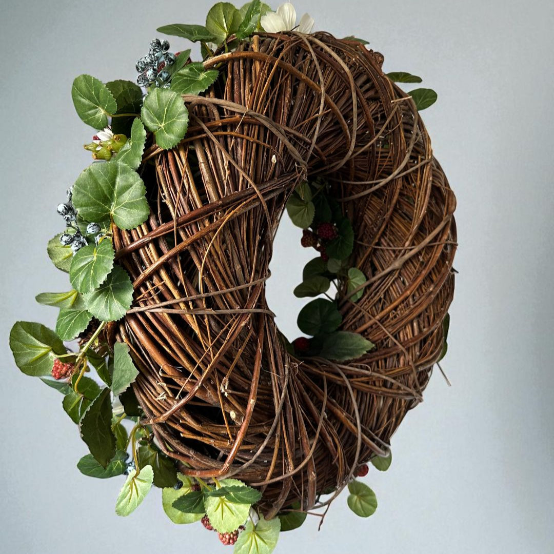 Woven wreath with green leaves and berries on a light gray background