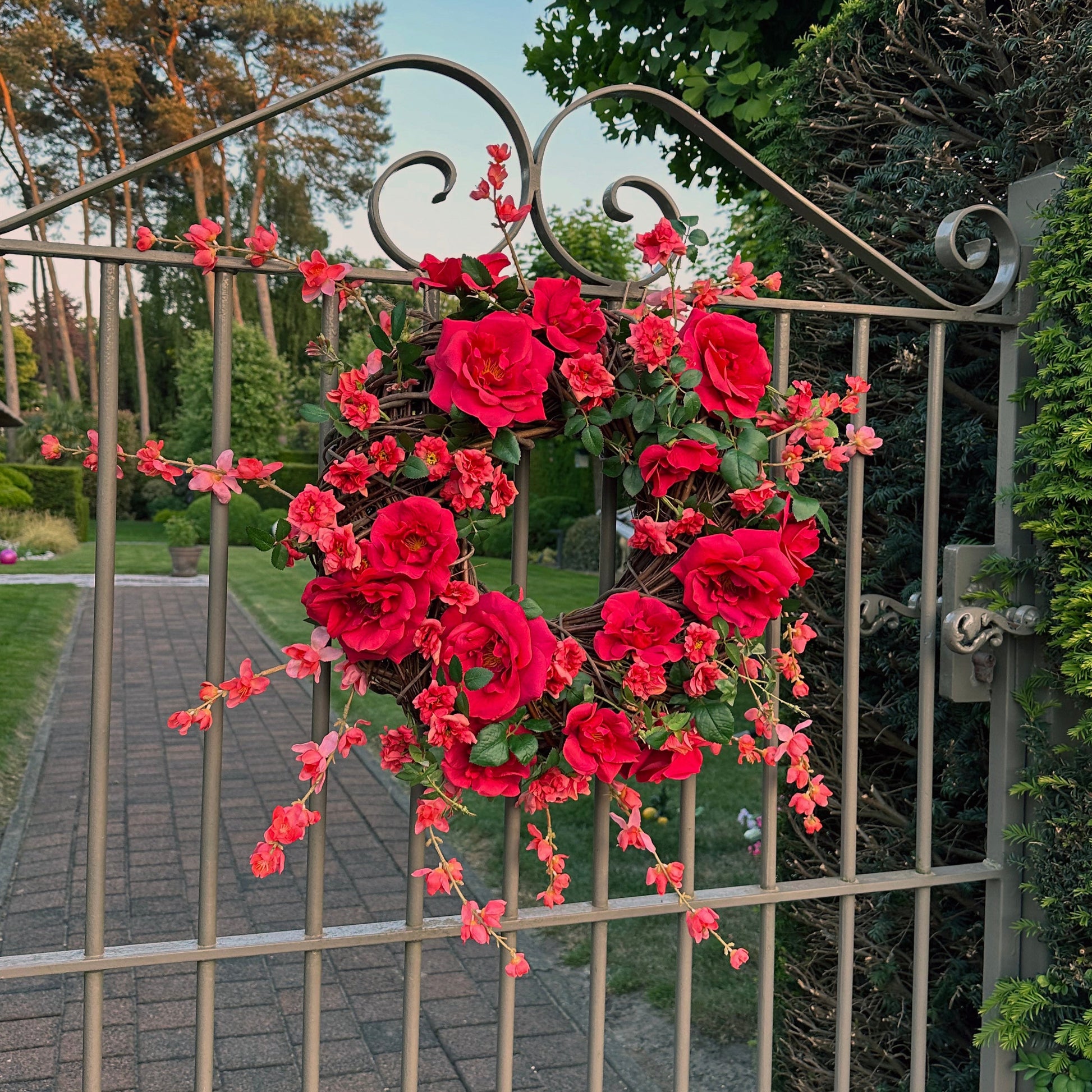 Handgemaakte luxe deurkrans met felle rode en fuchsia kunstrozen, delicate kersenbloesems en levendig groen blad, speels en asymmetrisch gerangschikt op een natuurlijke basis van takken. Deze expressieve bloemenkrans van Jardin Enchanté straalt passie, romantiek en mediterrane flair uit. Perfect als opvallende kunstbloemenkrans voor de voordeur, muurdecoratie of feestelijke gelegenheden. Ideaal voor wie een elegante, luxe seizoensdecoratie zoekt die direct een statement maakt.