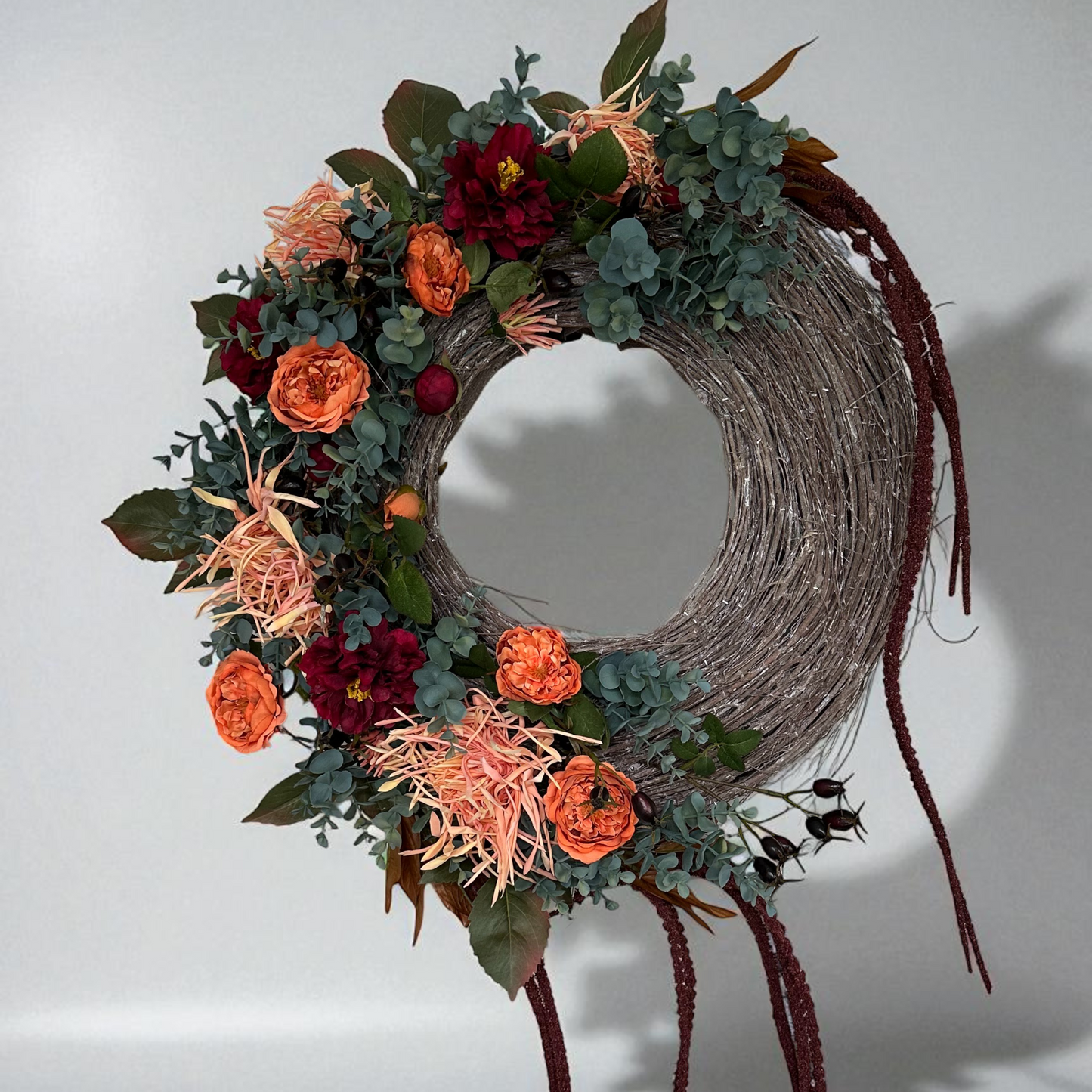 Elegant Falling Roses Wreath with orange roses, burgundy blooms, eucalyptus, and wilted spider mum flowers on a rustic twig base