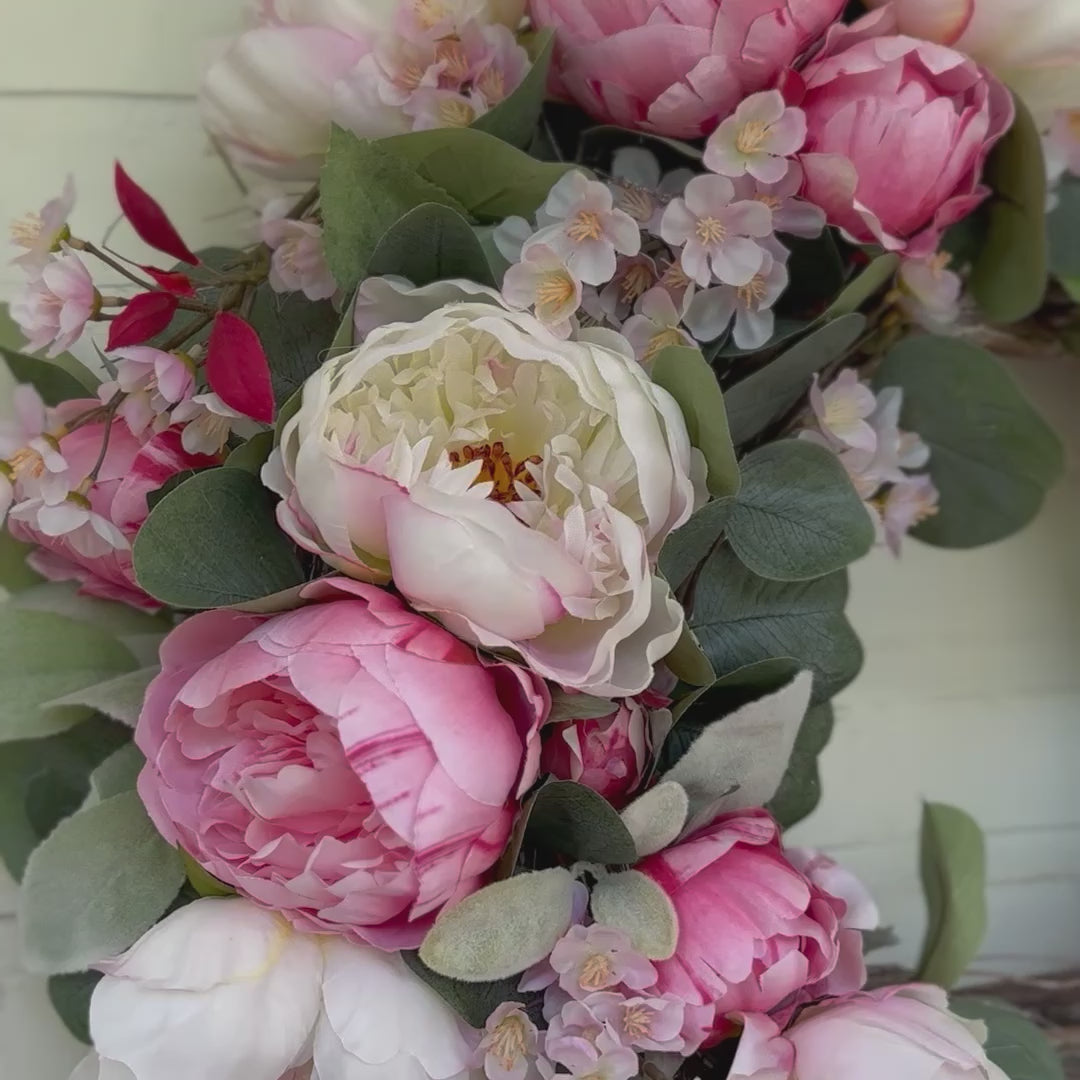Handgemaakte luxe deurkrans met zijden pioenrozen in zachte blushroze en crèmekleurige tinten, gecombineerd met kunst kersenbloesems en fluweelachtig groen blad, zorgvuldig gerangschikt op een natuurlijke takkenbasis. Deze romantische, asymmetrische bloemenkrans van Jardin Enchanté straalt Franse elegantie en verfijnde charme uit. Perfect als luxe kunstbloemenkrans voor de voordeur, muurdecoratie of feestelijke gelegenheid, en ideaal voor liefhebbers van romantische, exclusieve seizoensdecoratie.