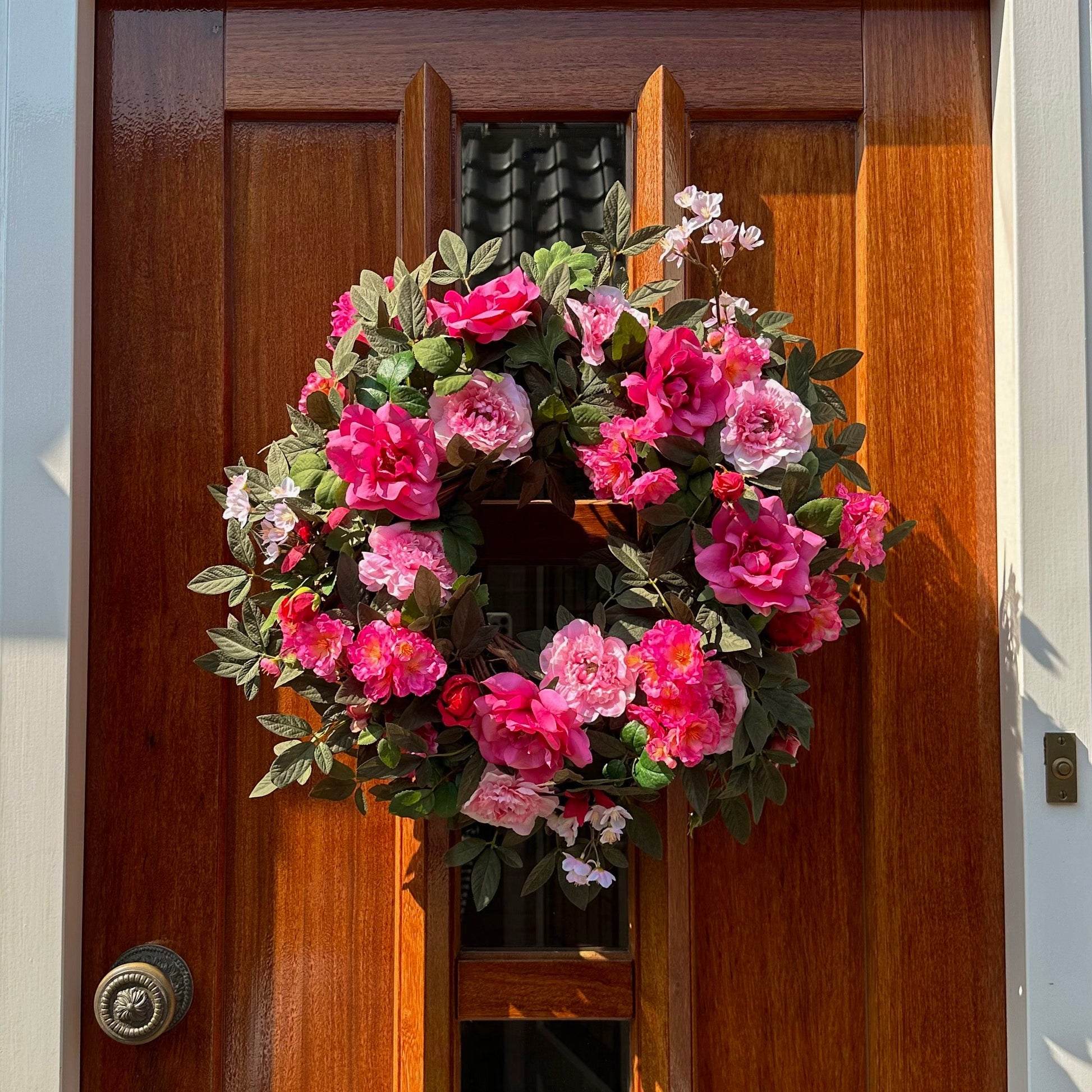 Handgemaakte luxe deurkrans met roze en fuchsia kunstrozen, pioenrozen en ranonkels op een groene, natuurlijke ondergrond — Jardin Enchanté.