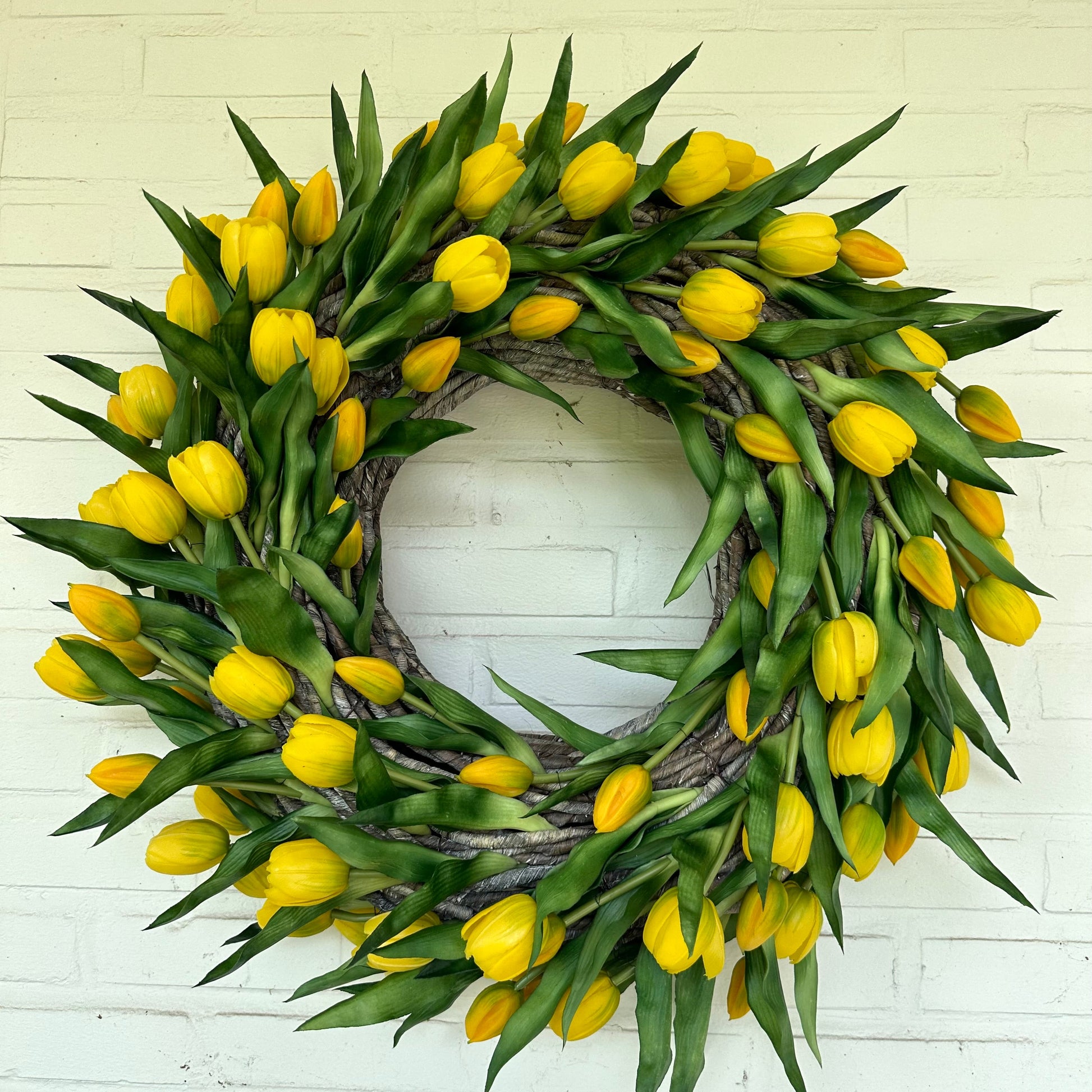 Handgemaakte luxe deurkrans met heldere gele kunsttulpen, kunstig gerangschikt op een natuurlijke, gevlochten takkenbasis. Deze opvallende tulpenkrans van Jardin Enchanté brengt direct zonneschijn en een warme, vrolijke uitstraling naar uw voordeur of interieur. Perfect als seizoensdecoratie voor de lente en zomer, en ideaal voor wie op zoek is naar een unieke luxe kunstbloemenkrans of stijlvolle deurdecoratie. Deze exclusieve krans combineert elegantie en levendige kleuren om een uitnodigende en verfijnde 