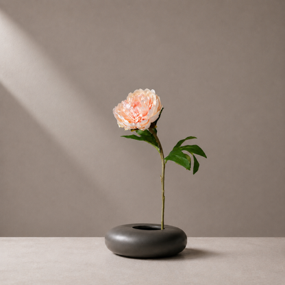 Premium velvet peach peony stem styled in a sculptural black vase against a warm neutral background