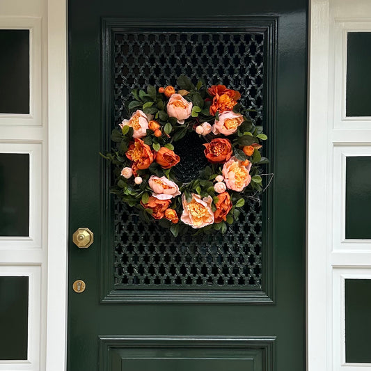 Herfst deurkrans met perzik en amberkleurige pioenrozen en groen blad, opgehangen aan een donkergroene voordeur. Handgemaakte bloemenkrans – stijlvolle herfstdecoratie voor de voordeur of interieur.