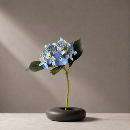 Real touch blue hydrangea stem styled in a sculptural black vase against a warm neutral background