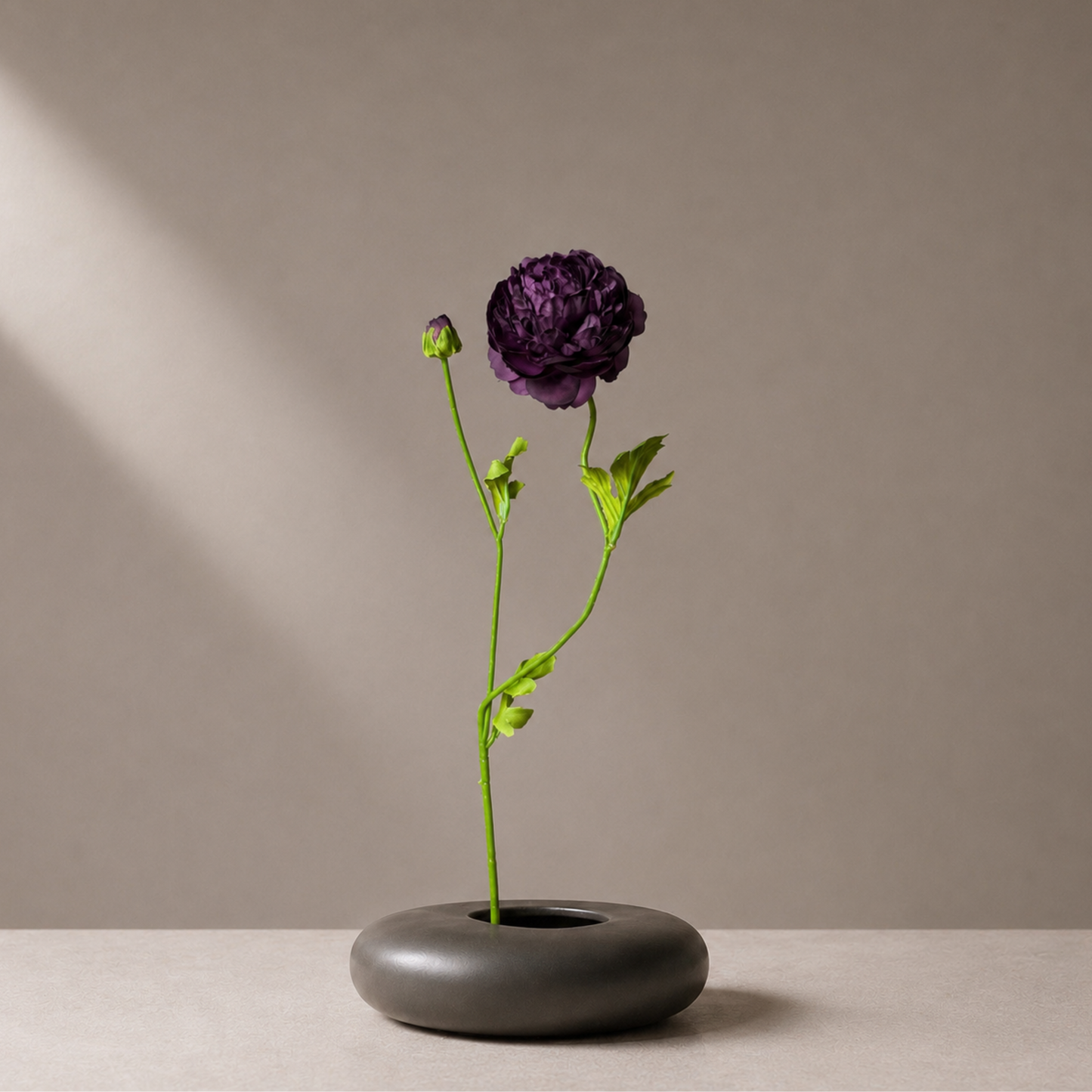 Real touch burgundy ranunculus stem styled in a sculptural black vase against a warm neutral background