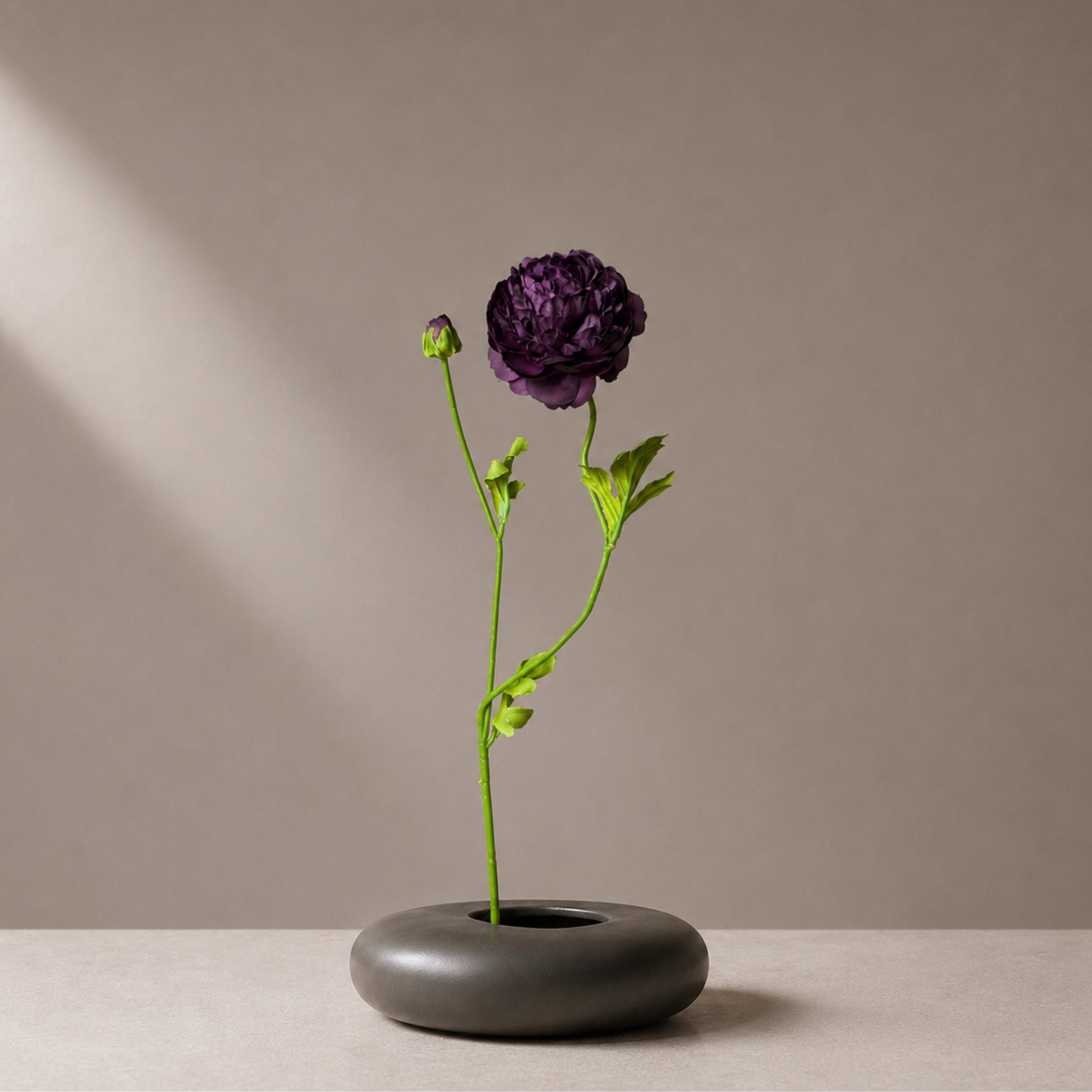 Real touch burgundy ranunculus stem styled in a sculptural black vase against a warm neutral background