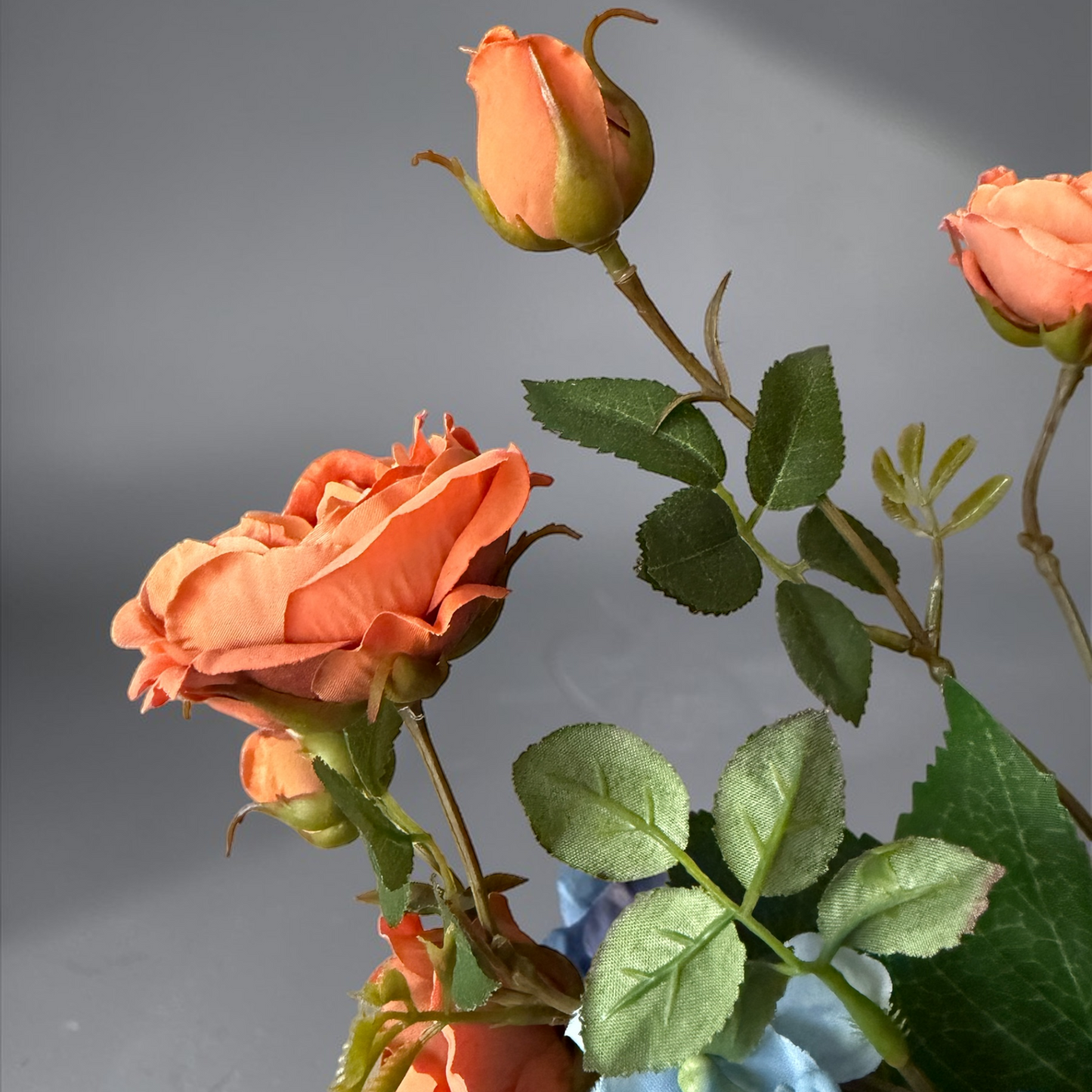 Luxury Burnt Apricot & Blue Mini Bouquet with silk orange garden roses and blue hydrangeas arranged in a white vase on a side table