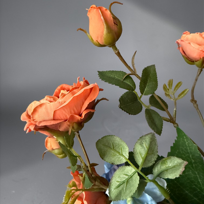 Luxury Burnt Apricot & Blue Mini Bouquet with silk orange garden roses and blue hydrangeas arranged in a white vase on a side table