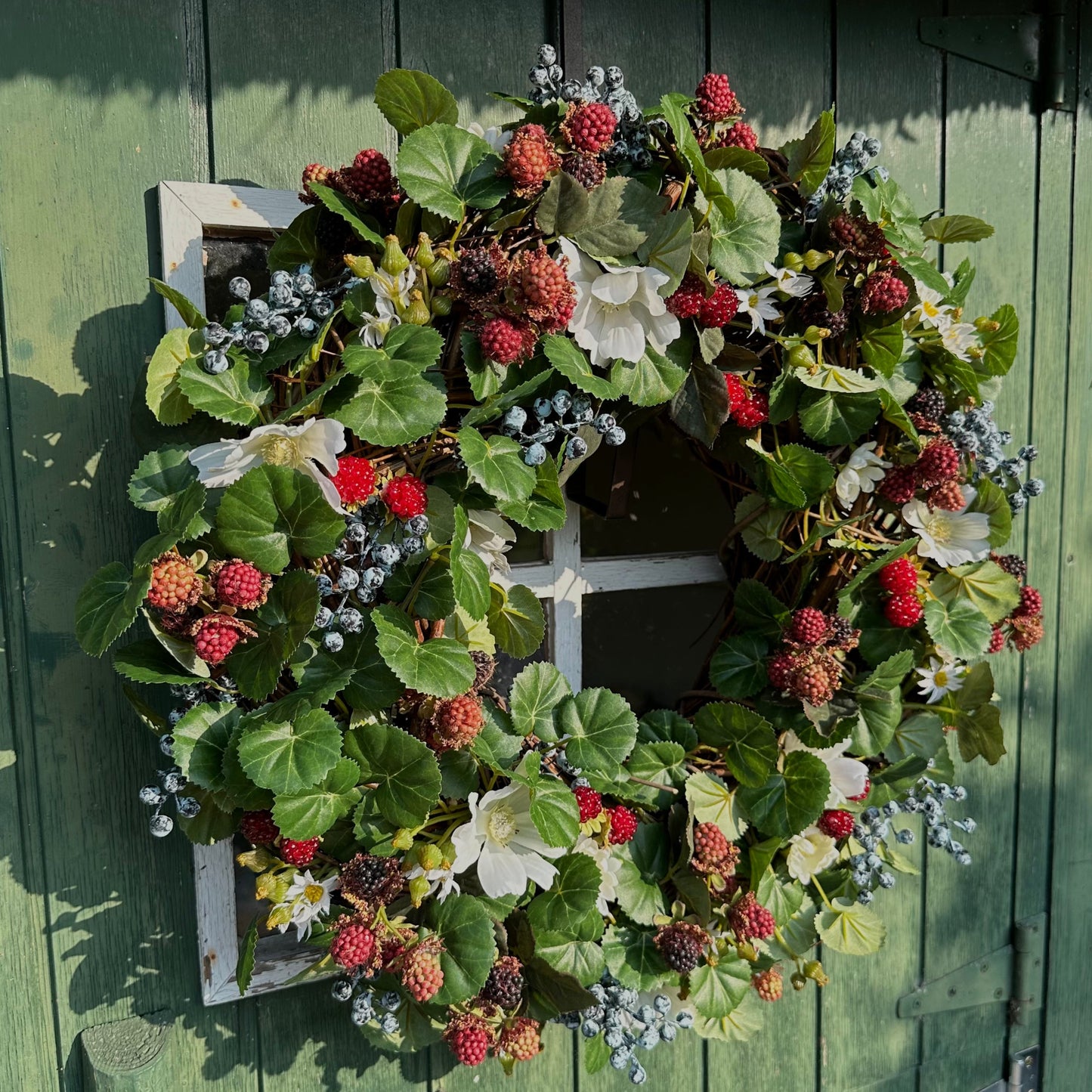 Handgemaakte luxe deurkrans met kunstzwarte bessen, frambozen, blauwe bessen, witte bloemen en rijk groen blad, kunstig gerangschikt op een natuurlijke, gevlochten takkenbasis. Deze betoverende boskrans van Jardin Enchanté brengt een elegante, wilde en sprookjesachtige uitstraling aan je voordeur of interieur. Perfect als seizoensdecoratie voor zomer en herfst, en ideaal voor liefhebbers van luxe kunstbloemenkransen en exclusieve deurdecoraties. Deze natuur geïnspireerde krans creëert een warme, poëtische s