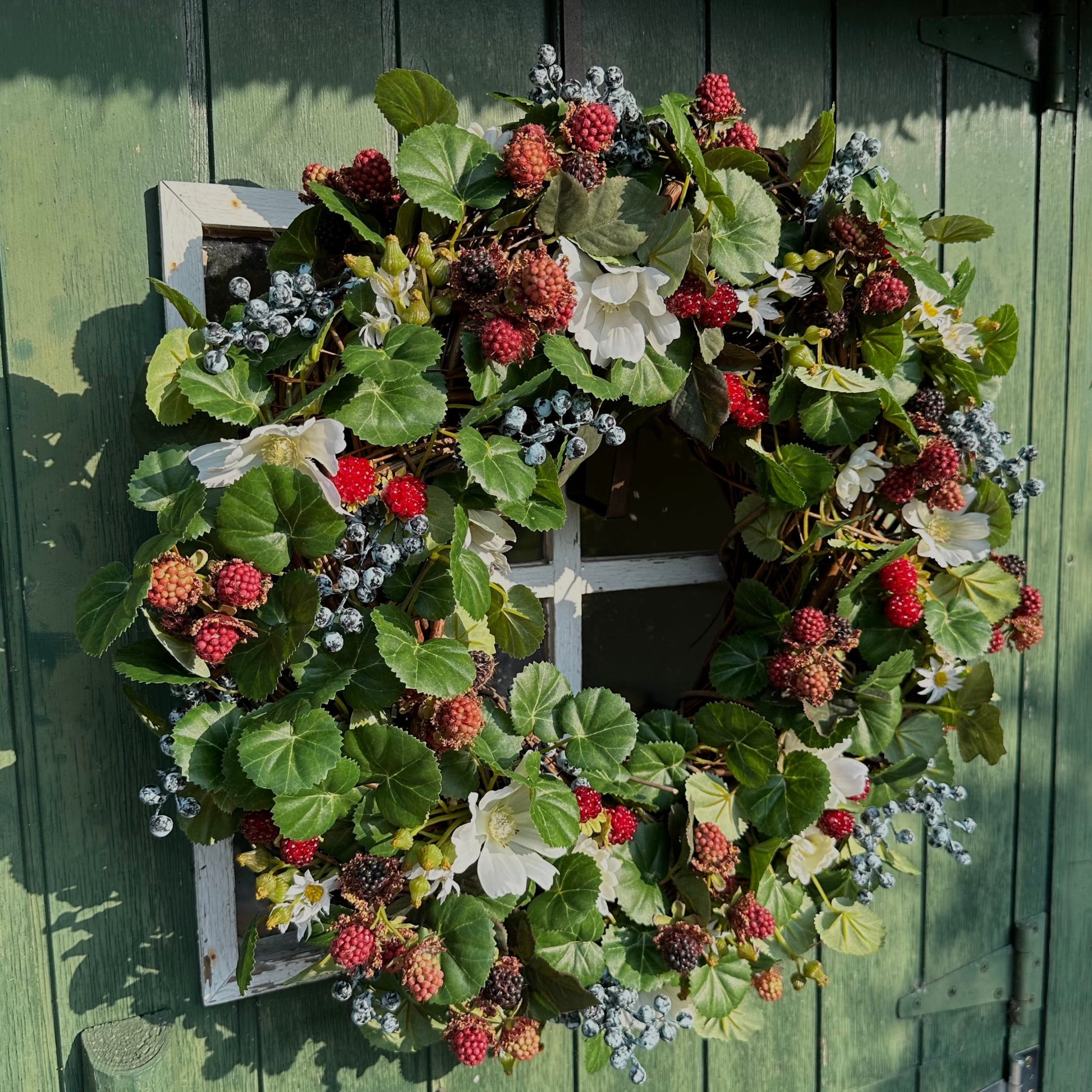 Handgemaakte luxe deurkrans met kunstzwarte bessen, frambozen, blauwe bessen, witte bloemen en rijk groen blad, kunstig gerangschikt op een natuurlijke, gevlochten takkenbasis. Deze betoverende boskrans van Jardin Enchanté brengt een elegante, wilde en sprookjesachtige uitstraling aan je voordeur of interieur. Perfect als seizoensdecoratie voor zomer en herfst, en ideaal voor liefhebbers van luxe kunstbloemenkransen en exclusieve deurdecoraties. Deze natuur geïnspireerde krans creëert een warme, poëtische s
