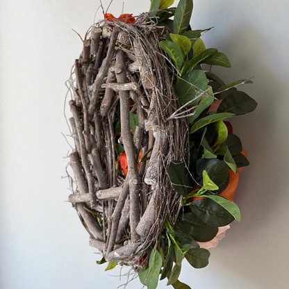 Side view of a handmade floral wreath with peach and burnt orange peonies, arranged on a natural grapevine twig base with lush green foliage. Rustic and elegant seasonal wreath design, showcasing craftsmanship and premium quality materials for front door or home décor.