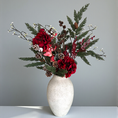 Luxe winterboeket met rode pioenrozen, dennentakken en dennenappels, handgemaakt door Jardin Enchanté. Elegant kunstbloemen boeket voor kerst en winterdecoratie, met natuurlijke uitstraling en warme seizoenskleuren. Perfect voor stijlvolle interieurdecoratie of als feestelijk cadeau.