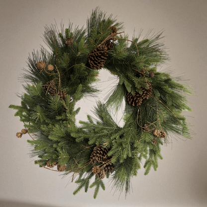 Luxe kunstkerstkrans met dennenappels en groen, stijlvol opgehangen aan een moderne voordeur — perfecte duurzame kerstdecoratie voor buiten.