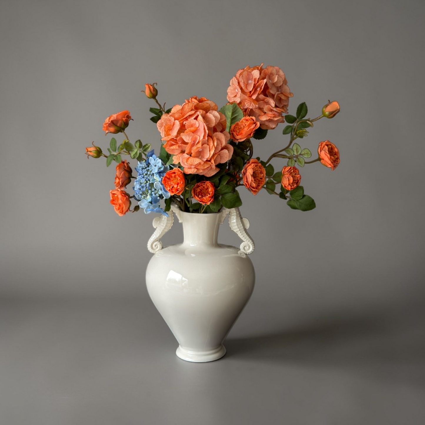 Luxe Burnt Apricot & Blue Mini Boeket met zijden oranje tuinrozen en blauwe hortensia’s in een witte vaas op een bijzettafel