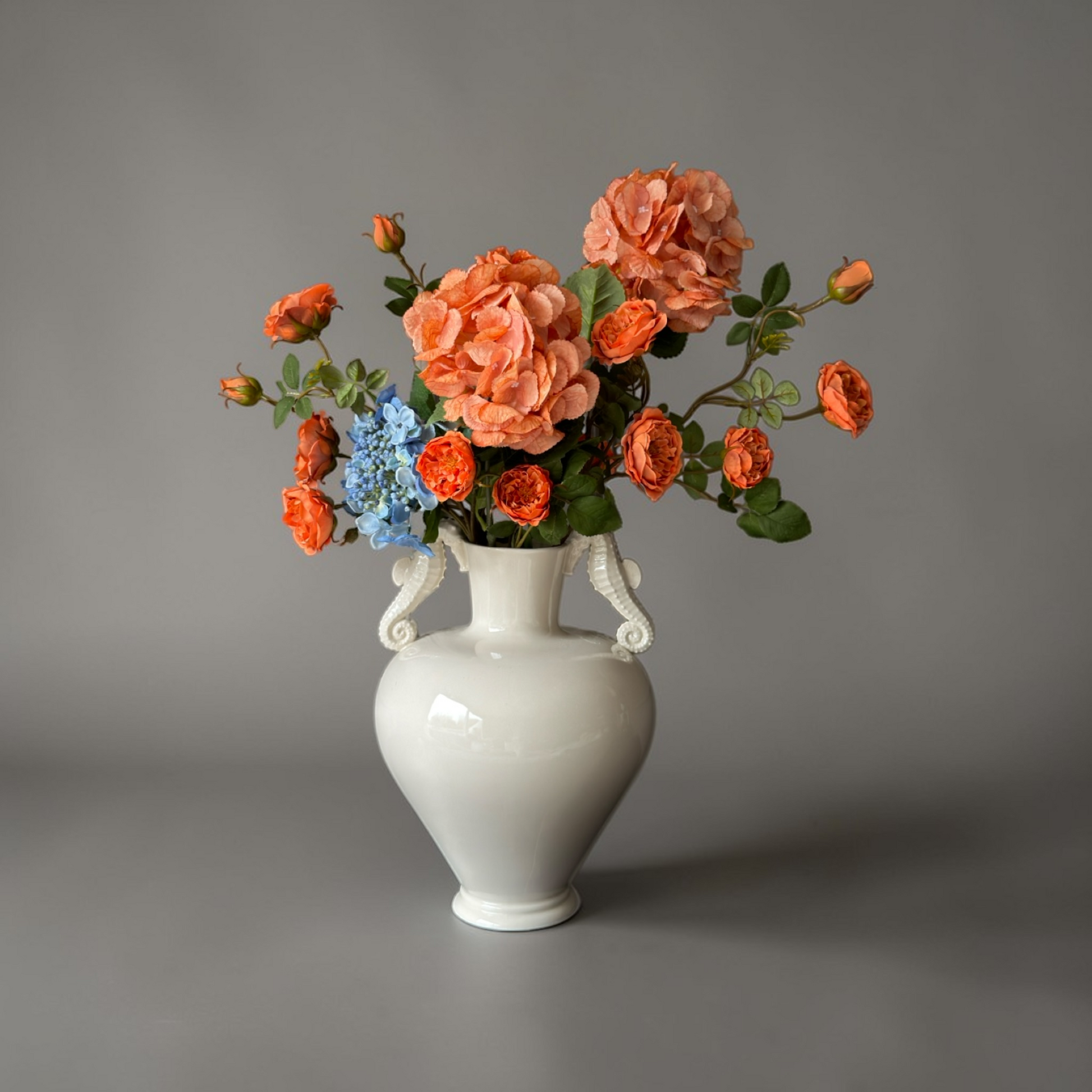 Luxe Burnt Apricot & Blue Mini Boeket met zijden oranje tuinrozen en blauwe hortensia’s in een witte vaas op een bijzettafel