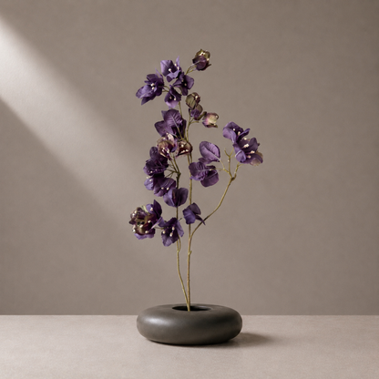 Premium artificial purple bougainvillea stem styled in a sculptural black vase against a warm neutral background