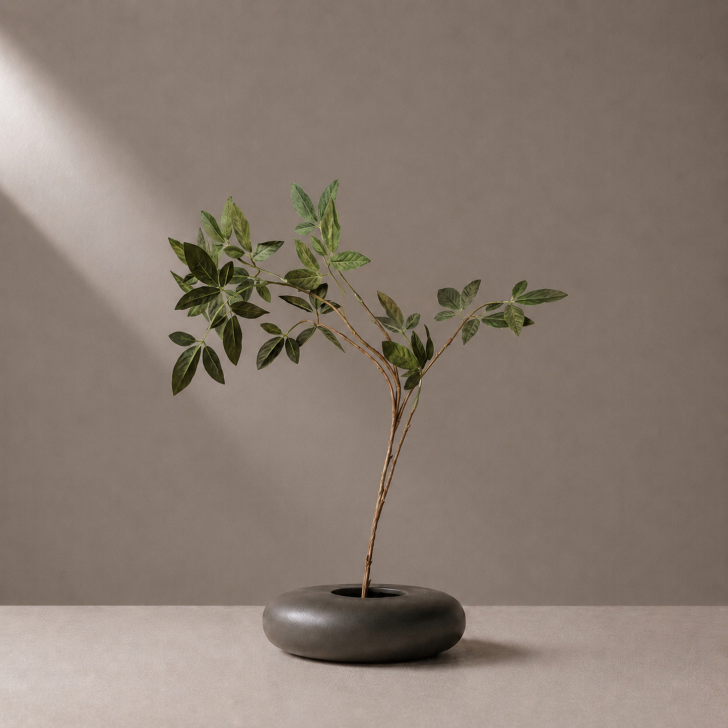 Premium artificial green leaf spray stem styled in a sculptural black vase against a warm neutral background