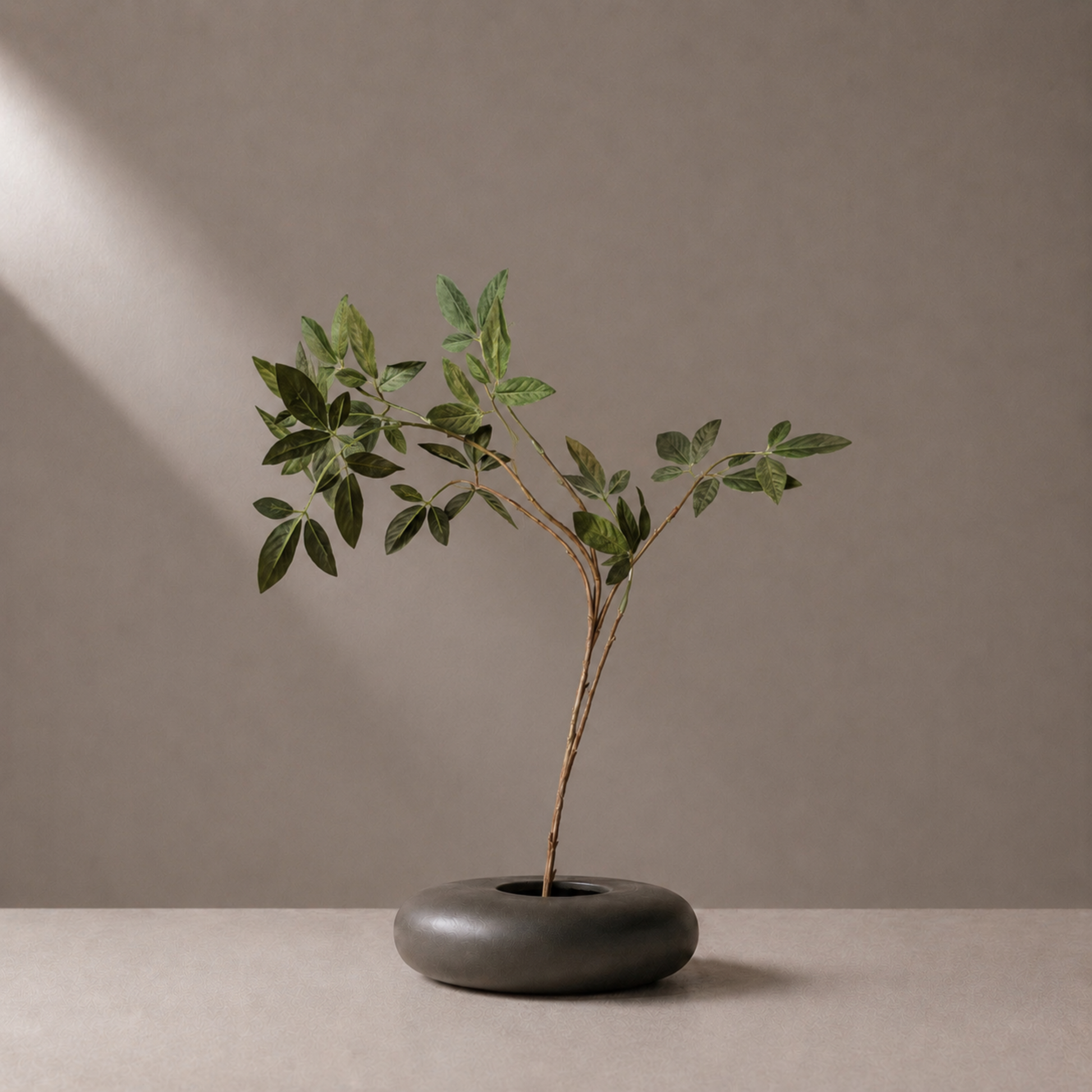 Premium artificial green leaf spray stem styled in a sculptural black vase against a warm neutral background
