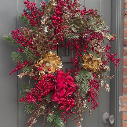 Luxe kunstkerstkrans met rode bessen, gouden bloemen en dennetakken, opgehangen aan een moderne grijze voordeur – stijlvolle kerstdecoratie met feestelijke uitstraling.