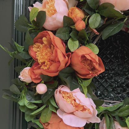 Herfst deurkrans met perzik en amberkleurige pioenrozen en groen blad, opgehangen aan een donkergroene voordeur. Handgemaakte bloemenkrans – stijlvolle herfstdecoratie voor de voordeur of interieur.