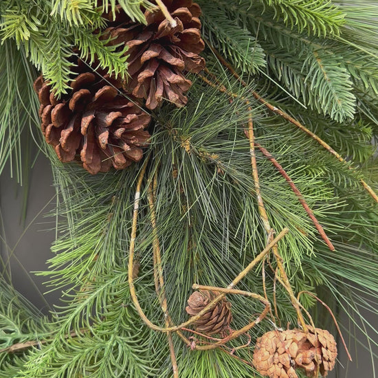 Luxe kunstkerstkrans met dennenappels en groen, stijlvol opgehangen aan een moderne voordeur — perfecte duurzame kerstdecoratie voor buiten.