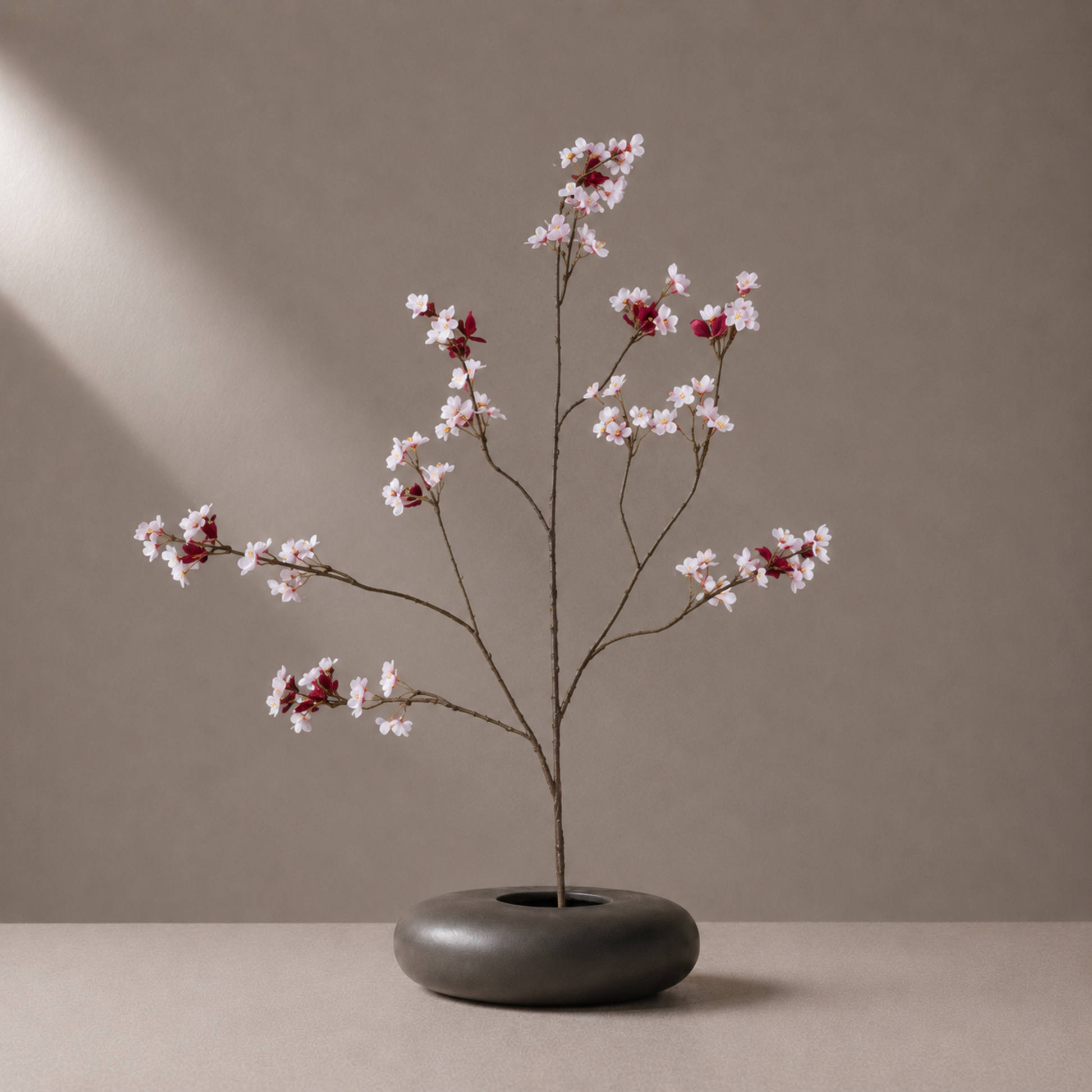 Real touch pink peach blossom spray branch styled in a sculptural black vase against a warm neutral background