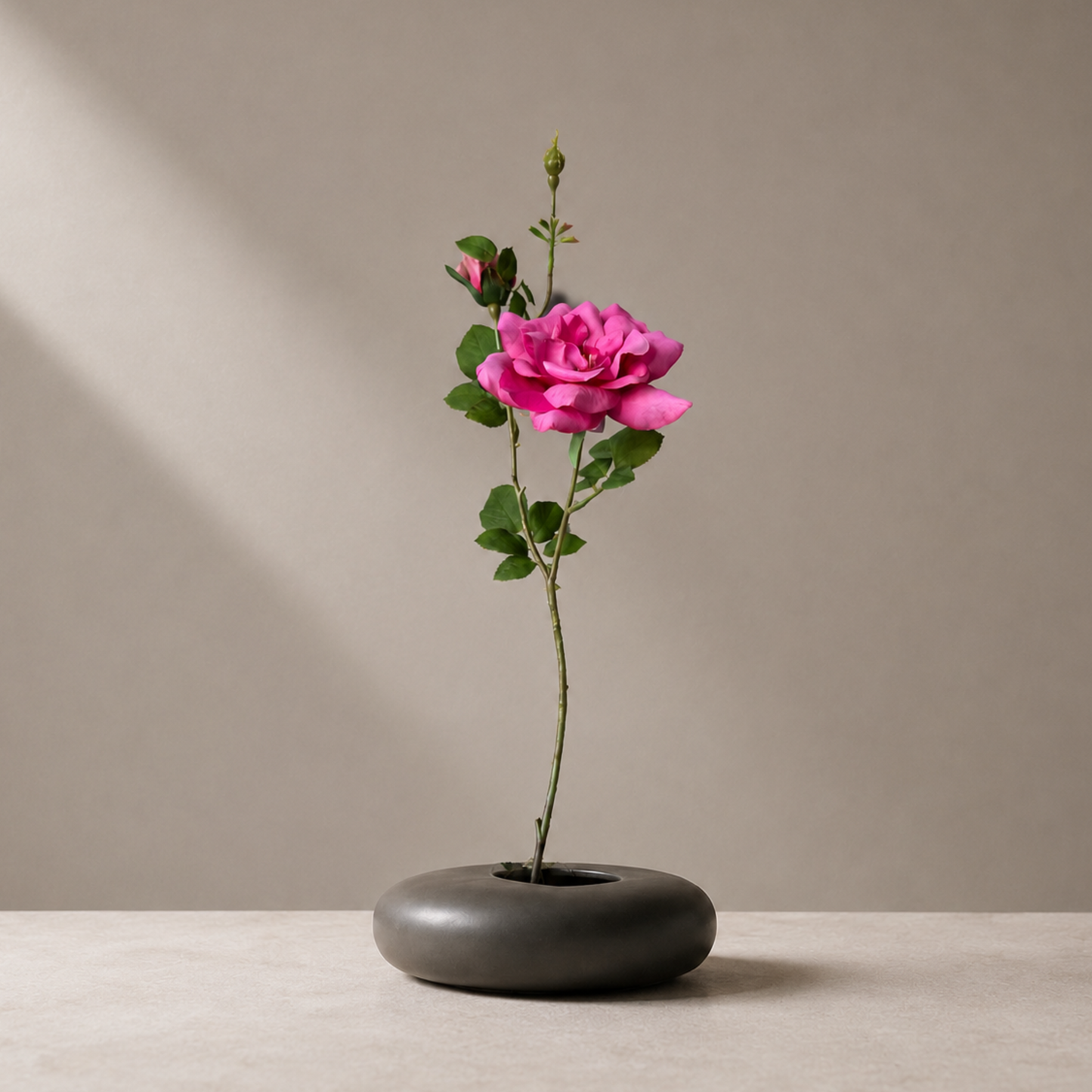 Real touch pink garden rose stem in a sculptural black vase against a soft neutral background