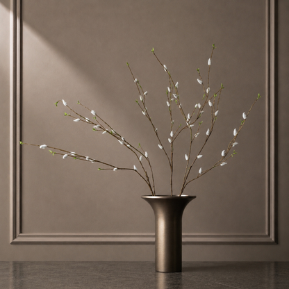 Arrangement of real touch pussy willow branches in a sculptural dark vase against a warm neutral background