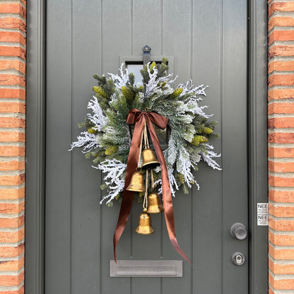 Stijlvolle kunstkerstkrans met gouden belletjes en bruine satijnen strik, opgehangen aan een moderne grijze voordeur – luxe winterdecoratie voor buiten