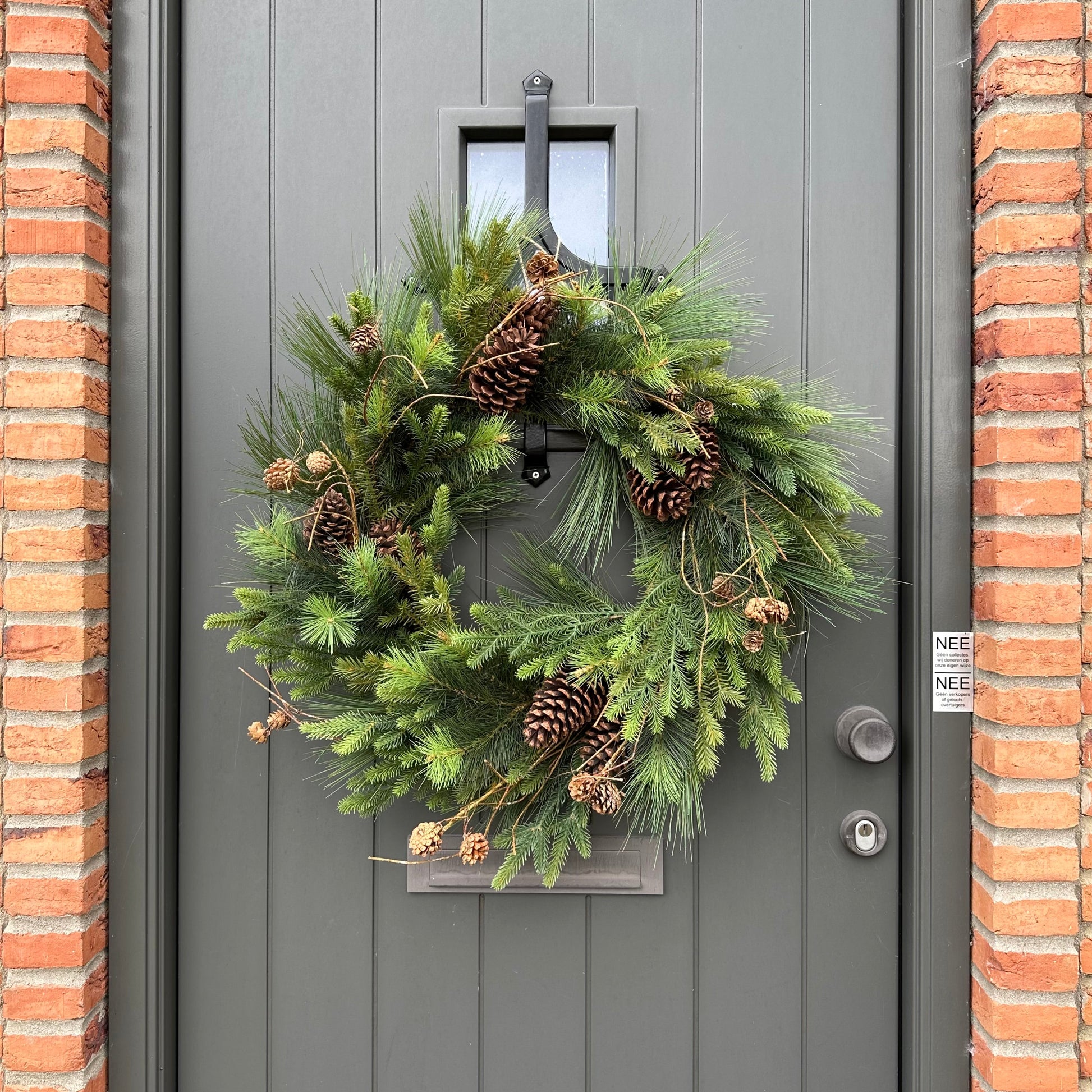 Luxe kunstkerstkrans met dennenappels en groen, stijlvol opgehangen aan een moderne voordeur — perfecte duurzame kerstdecoratie voor buiten.