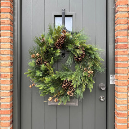 Luxe kunstkerstkrans met dennenappels en groen, stijlvol opgehangen aan een moderne voordeur — perfecte duurzame kerstdecoratie voor buiten.