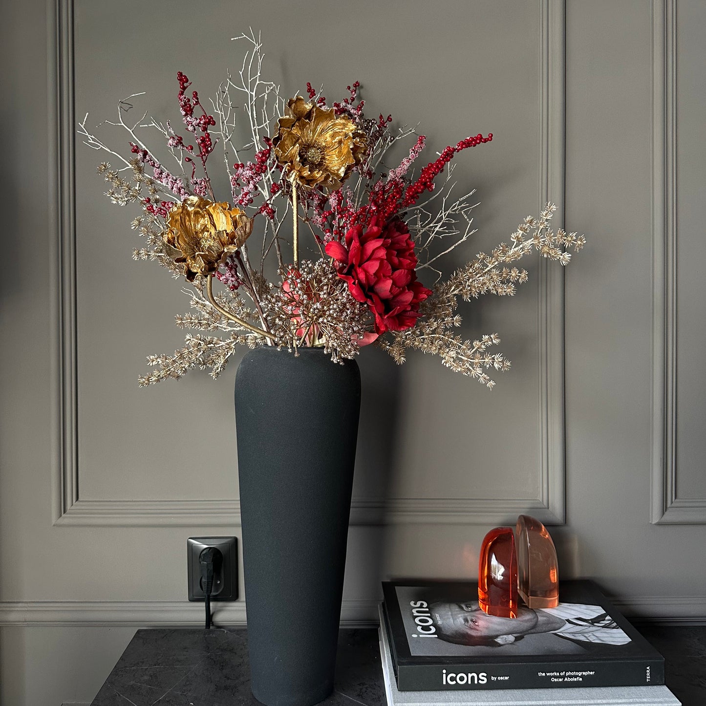 Luxe winterboeket van kunstbloemen met dieprode pioenrozen, gouden papaverbloemen en wintergroen in een stijlvolle vaas – perfecte decoratie voor feestdagen en interieur.