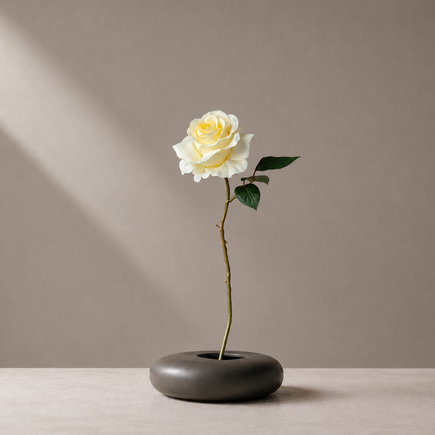 Real touch yellow rose stem styled in a sculptural black vase against a warm neutral background