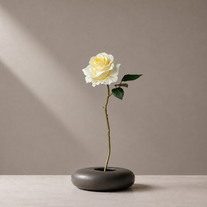 Real touch yellow rose stem styled in a sculptural black vase against a warm neutral background
